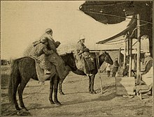 photographie ancienne, d'un couple chacun sur son cheval avec un enfant, devant un commerce