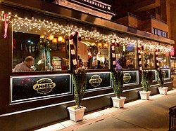 Exterior of a restaurant at night, with white holiday lights and signage under each window reading "Annie's"