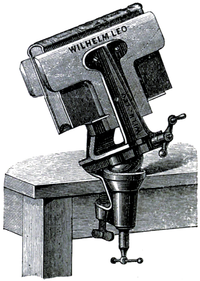 Cross-hatched illustration of a vice, clamped to the edge of a desk, holding a book tightly closed.