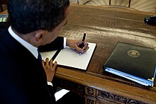 Barack Obama signs at his desk.jpg