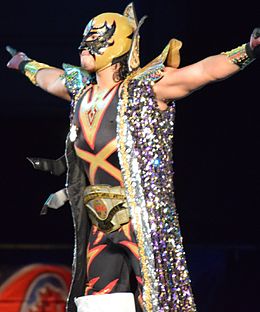 O lutador mascarado Máscara Dorada posando com um cinto do campeonato enrolado na cintura