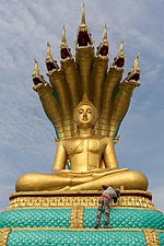 Travailleur peignant couleur or une statue géante du Buddha assis, au temple de Don Loppadi. Janvier 2018.