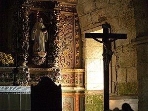 Crucifix situé devant une fenêtre latérale et un retable baroque.