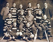 An ice hockey team poses for a photo, with ten players in uniforms and three men in suits