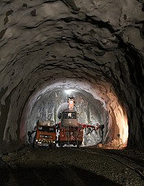A tunnel under construction by conventional excavation methods with a pilot tunnel through tunnel face and a drill jumbo positioned near the face. Rock engineers and geotechnical engineers (subdisciplines of geological engineering) are involved with the design and construction of underground excavations. Pilot Tunnel High Res.jpg