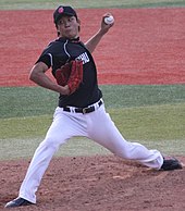 Yūdai Ōno na sobě námořnickou baseballovou uniformu a námořní čepici v procesu pitching baseball