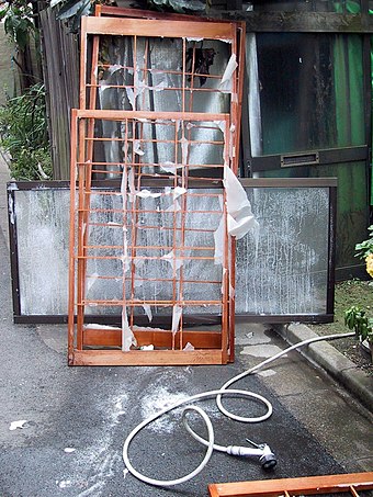 Wet shoji frame with a few rags of paper clinging to it, and a showerhead, just outdoors.