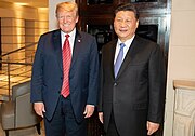 Donald Trump dan Xi Jinping berdiri di samping satu sama lain, keduanya tersenyum dan mengenakan pakaian