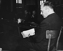 Priest Friedrich Hoffman testifies at the trial of former camp personnel and prisoners from Dachau. In his hand he holds records showing that hundreds of priests died at the camp after being exposed to malaria during Nazi medical experiments. Friedrich Hoffmann priest.jpg