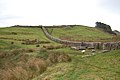 Blick vom Hadrianswall nach Westen auf einen kleinen Limesdurchgang rechts. Auf der Hügelkuppe liegt Kastell Housestead.