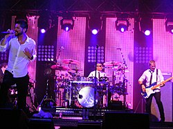INXS performing in white shirts over a pink-lighted stage.