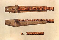 En lang og tynn kanon montert på en massiv treramme av et enkelt stykke tre, sett fra oven og fra siden