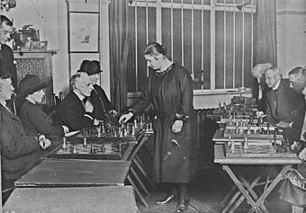 After Menchik won the 1926 London Girls' Championship, she gave a 13-board simultaneous exhibition (pictured) at the event, scoring +9-2=2. Miss Menchik jouant aux echecs (cropped).jpg