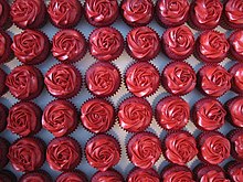 a photograph taken from above rows of red velvet cupcake in red paper liners with red frosting