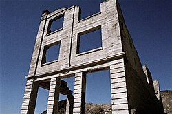 Ruins of a three-story masonry building rise into a dark, cloudless blue sky. The building lacks a roof, and its windows have no glass.
