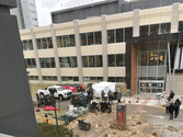 A university building with people, equipment, and a vehicle in the foreground.