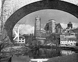 Historická černobílá fotografie zobrazující kostel sv. Michala pod obloukem mostu
