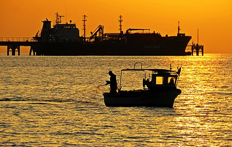 Fisherman laying his nets while the merchant ship stops at the pier