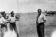 L'asso Heinrich Heinz Bär (a destra), comandante del I./JG 77. La foto è stata probabilmente scattata nel luglio 1942 a Comiso, in Italia. Sulla sinistra si può notare la coda di un Bf 109F-4, sul cui timone è riportato il numero 40 circondato da foglie, ad indicare il raggiungimento delle 40 vittorie. Bär all'epoca aveva già superato le 100 vittorie e concluse la guerra a quota 220.