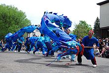 people watching about seven street dancers with a large blue dragon puppet
