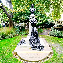 Colour photo of bronze statue of a partly-clothed muse, leaning on a stone pillar, looking up, longingly, at a bronze bust of Sullivan