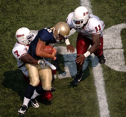 College football game: Navy quarterback Kaipo-Noa Kaheaku-Enhada (blue) is tackled by Massachusetts defensive back James Ihedigbo, (white 7), and linebacker Charles Walker, (white 11).