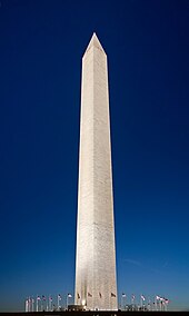 A dusk picture of the Washington Monument obelisk with flags around the base, in Washington, D.C.