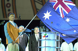 Robert Steadward (right rear) looks on as the Australian flag is brought to the stage by flagbearer Brendan Burkett during the opening ceremony of the 2000 Sydney Paralympic Games. 201000 - Opening Ceremony swimmer Brendan Burkett flag - 3b - 2000 Sydney opening ceremony photo.jpg