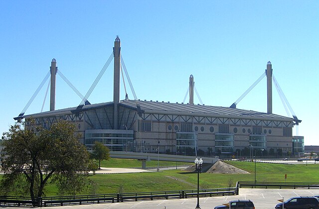 A building with four towers that raise high above the building and each have three sets of suspension cabling connected to the roof of the building.