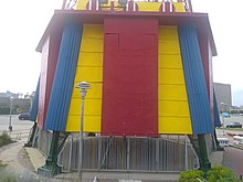 The pavilion, a two-story building painted red, yellow, and blue. A metal gate is at the front.