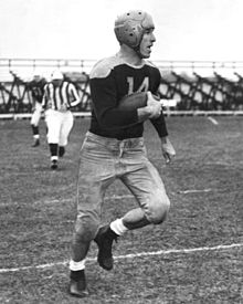 Don Hutson in a Green Bay Packers uniform carrying the ball down a football field.