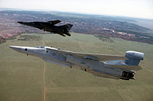 An EF-111A Raven in the foreground with a tail-mounted receiving pod and an underside-mounted transmitting pod, accompanied by an F-111F