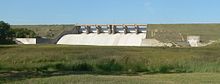 Concrete structure in grass-covered earthen dam; six floodgates