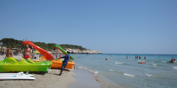 Man renting leisure boats on beach at Sant Tomas, Menorca pulling a boat towards the sea