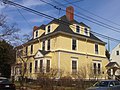 Une grande maison de style colonial jaune de 2 1/2 étages avec des garnitures blanches.