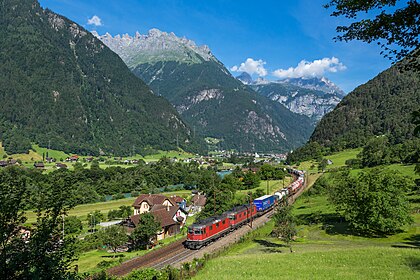 Uma locomotiva Re 4/4 II e uma Re 6/6 transportam um trem de carga intermodal para o sul na linha do Gotardo nos arredores de Erstfeld (visível ao fundo), Suíça. A série Re 420, originalmente (e ainda amplamente chamada) Re 4/4 II, são as locomotivas elétricas mais comuns das Ferrovias Federais Suíças. Elas são usadas ​​para serviços de passageiros em toda a Suíça, sozinhas ou em pares. Para serviços de carga, elas às vezes são combinadas com a Re 6/6, especialmente em regiões montanhosas. Esse emparelhamento é referido pelo termo Re 10/10. A Re 430, originalmente conhecida como Re 4/4 III, é uma derivada da Re 420 modificada para maior tração, mas menor velocidade. As locomotivas Re 420 foram produzidas ao longo de 21 anos, de 1964 a 1985. (definição 5 198 × 3 465)