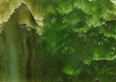 Le visage d'une dalle polie de serpentine bowénite avec un motif ondulé dans des couleurs allant du vert jade intense au jaune.