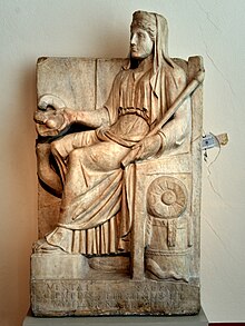 White marble votive relief of Vesta, Hestia's Roman equivalent. She is sitting down, with a veil covering her hair. In her left hand is a staff. In her right is a plate.