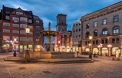 Caritasbrønden (Poço da Caridade) ao anoitecer, Copenhague, Dinamarca. É a fonte mais antiga de Copenhague, construída em 1608 na praça Gammeltorv em Strøget. A fonte foi construída por Cristiano IV sobre um dos poços da cidade e é considerada um dos melhores monumentos de Copenhague da Renascença. Na verdade, foi uma mudança e modernização de uma fonte mais antiga da época de Frederico II. A antiga fonte tinha um cano de água de madeira de 6 quilômetros de comprimento ligando o lago Emdrup a Gammeltorv, e como a diferença de nível entre o lago e a praça é de 9 metros, havia pressão de água suficiente para fazer uma fonte. Embora provavelmente fosse para decoração, o poço fazia parte do abastecimento normal de água da cidade. (definição 4 263 × 2 738)