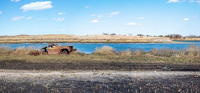 Aan de rand van een verloren pad, een lege opmars van water, in een landschap zonder bebouwing, een verlaten autowrak.