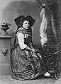 Fotografi fra 1870'erne af kvinde fra Alsace klædt i folkedragt ved en lille rok med højt rokhoved med uldfiber.