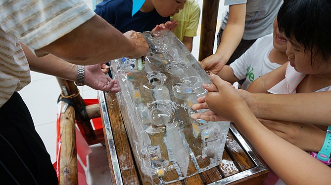 Children gather around a block of ice containing small toys.