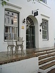 This property initially formed the boundary of the original Stellenbosch cemetery which fell into disuse in 1710. In 1783 the plot came into the ownership of J. B. Hoffman, who was presumably responsible for the erection of the original Cape Dutch house. This building was thereafter used as a boarding-house for many decades. By 1889 an additional storey had been added, which gave the building its present imposing Georgian appearance. D'Ouwe Werf entrance.JPG