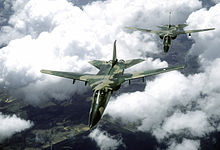 Front view of two jet aircraft in two-tone green camouflage scheme in-flight, wings unswept. The trailing aircraft is slightly off-centered to the right