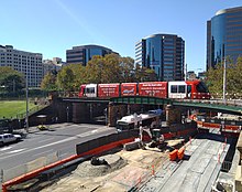 An Urbos 3 arrives at Central with a service on the Inner West Light Rail. A construction site for the CBD and South East Light Rail on Eddy Avenue is below. The bridge was originally constructed for Sydney's former tram network.