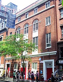 A red-brick three-story building with a tree outside it.