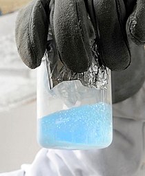 A transparent beaker containing a light blue fluid with gas bubbles
