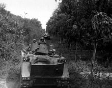United States Army M113 and M48A3 tank deploy along a road between the jungle and rubber plantation. M113 Jungle Convoy Vietnam War.jpg