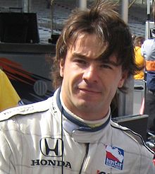 Servià è un uomo dai capelli scuri e dalla pelle bianca che qui indossa un completo IndyCar bianco.