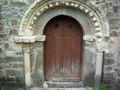 Puerta "del Cuerno" de Santa María de Piasca. La segunda dovela hacia la derecha de la clave contiene el relieve de dos cabezas, una barbada y otra imberbe, en actitud de iniciar un beso. Se ha interpretado como referencia al encuentro de Alfonso VIII de Castilla y Leonor Plantagenet (1170).[1]